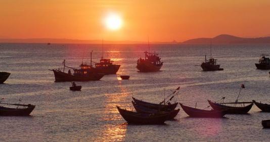 Bức tranh phong cảnh biển lúc hoàng hôn rực rỡ với mặt trời đỏ ối từ từ lặn xuống và những đám mây nhuộm màu cam vàng