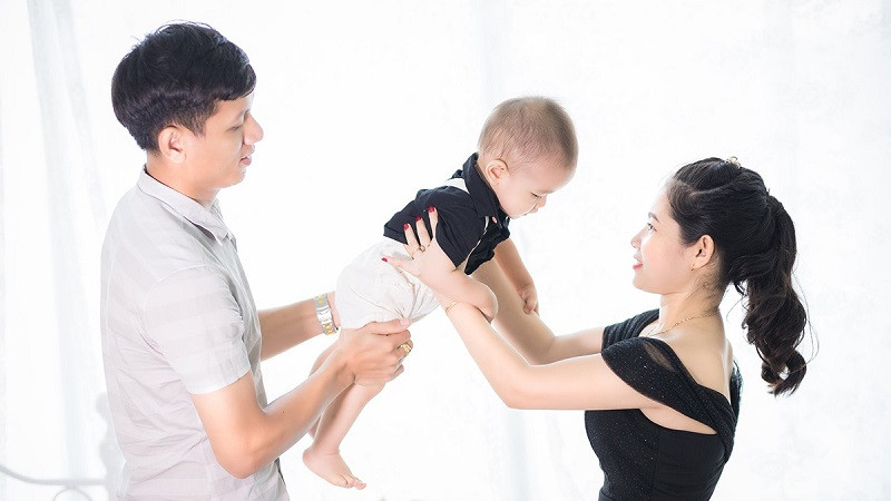 Bố bế con gái, mẹ ôm từ phía sau, cả nhà cười tươi