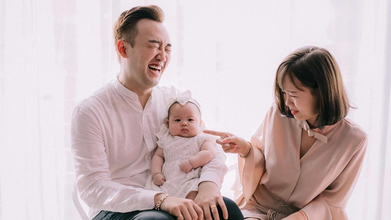 Bố bế con trai nhỏ, mẹ đứng cạnh cười tươi trong nhà