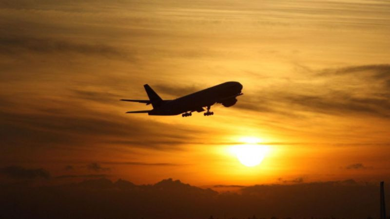 Cận cảnh một chiếc máy bay cánh quạt nhỏ đang cất cánh trên đường băng, phía sau là khu rừng và bầu trời quang đãng