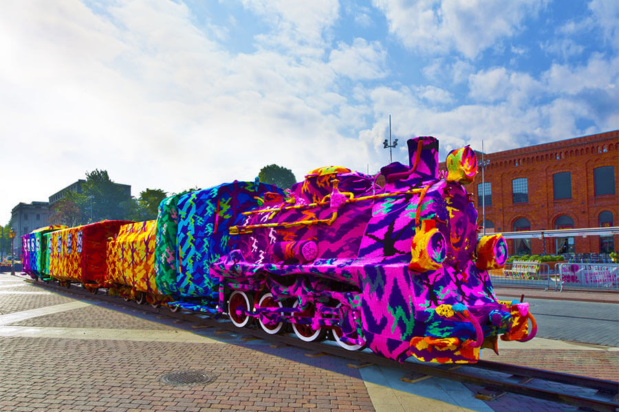 Cây cột được bao phủ bằng vải dệt nhiều màu sắc, ví dụ về Yarn Bombing trong nghệ thuật đường phố