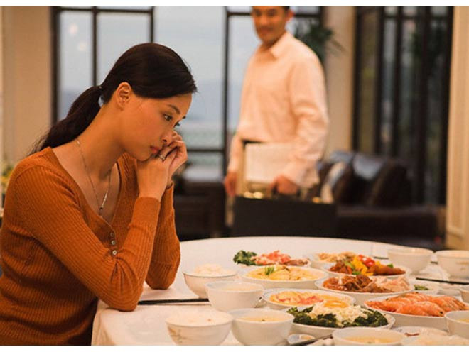 Cô gái ngồi một mình bên mâm cơm, thể hiện sự cô đơn trong gia đình