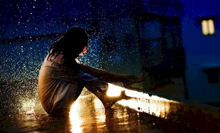 Cô gái trẻ đứng một mình dưới màn mưa, thể hiện sự cô đơn