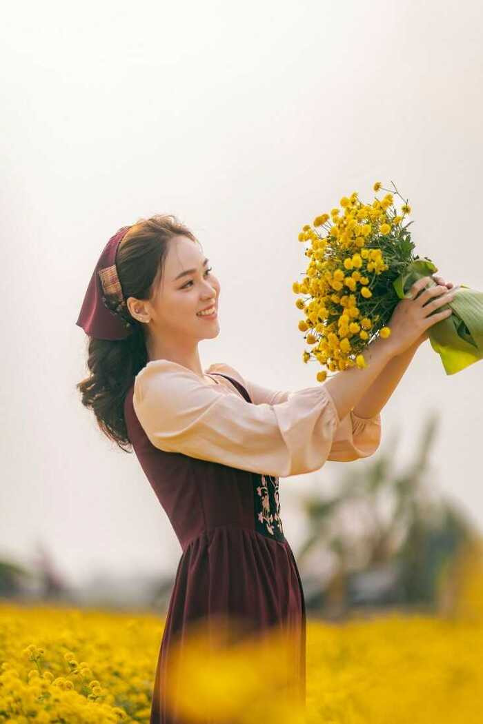 Cô gái trẻ trung cầm hoa cười rạng rỡ dưới ánh nắng