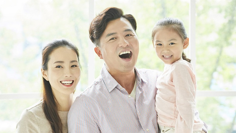 Gia đình 3 người mặc đồ đôi màu nâu nhạt, ngồi trên nền trắng