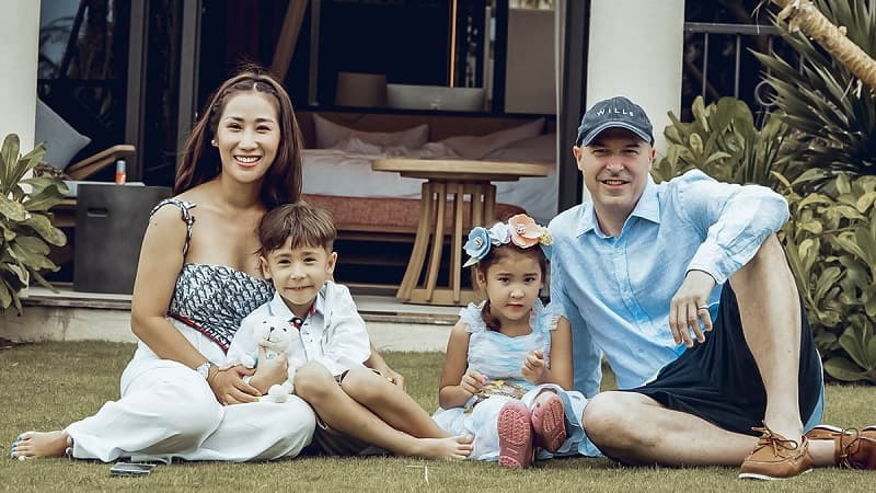 Gia đình 4 người mặc áo sơ mi xanh nhạt, ngồi trên ghế gỗ