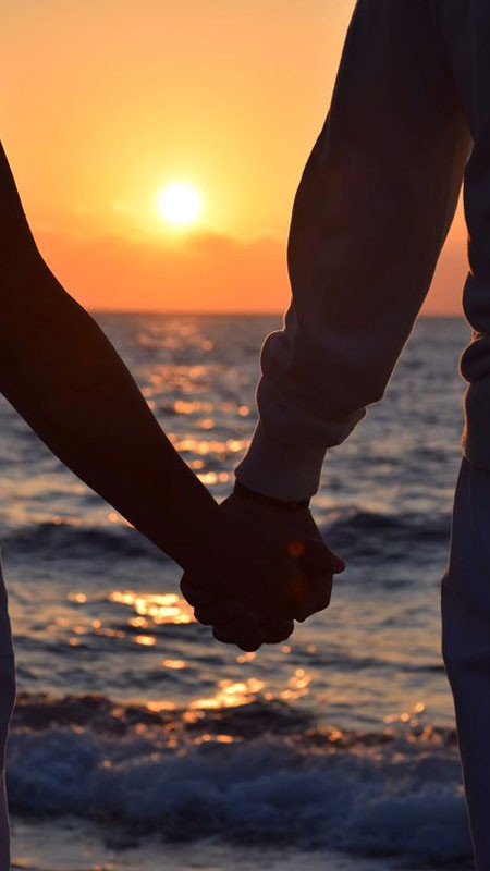 Góc nhìn từ phía sau, đôi lứa nắm tay đi về phía biển rộng