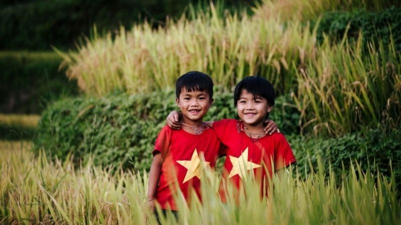 Hai cậu bé tươi cười mặc áo cờ đỏ sao vàng