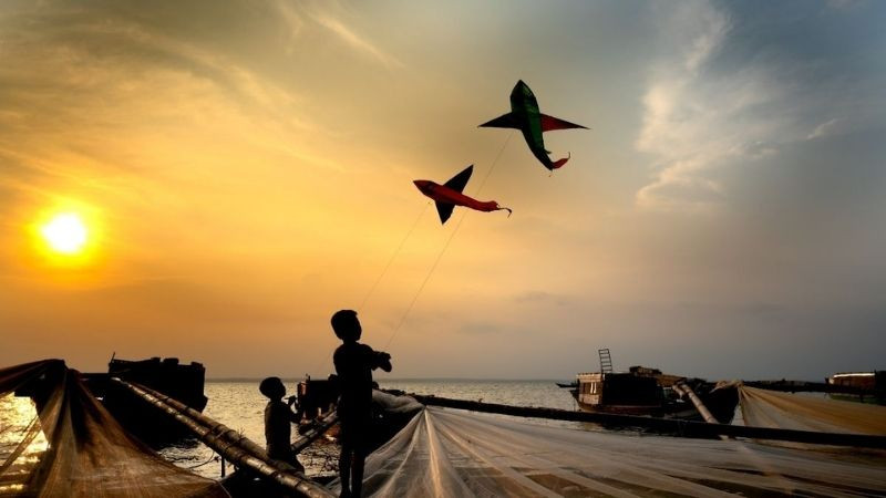 Hai đứa trẻ thả diều trên biển lúc hoàng hôn