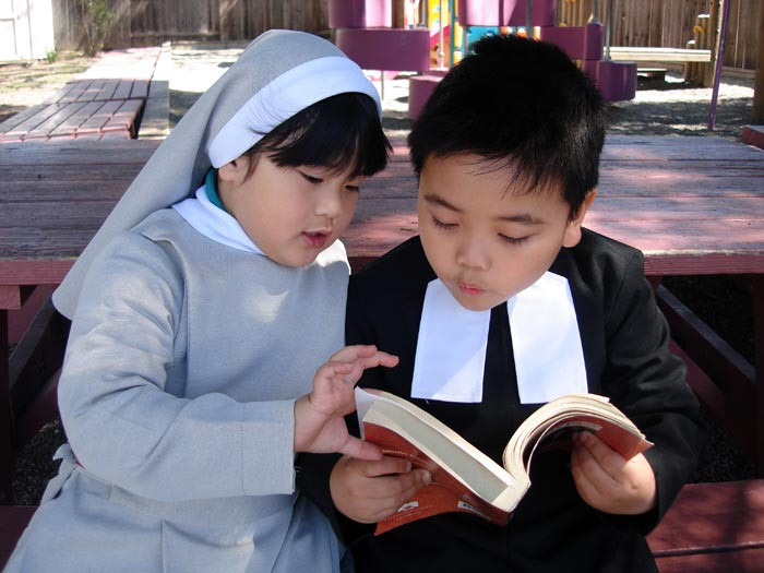 Hai em bé trong trang phục tu sĩ đọc sách cùng nhau