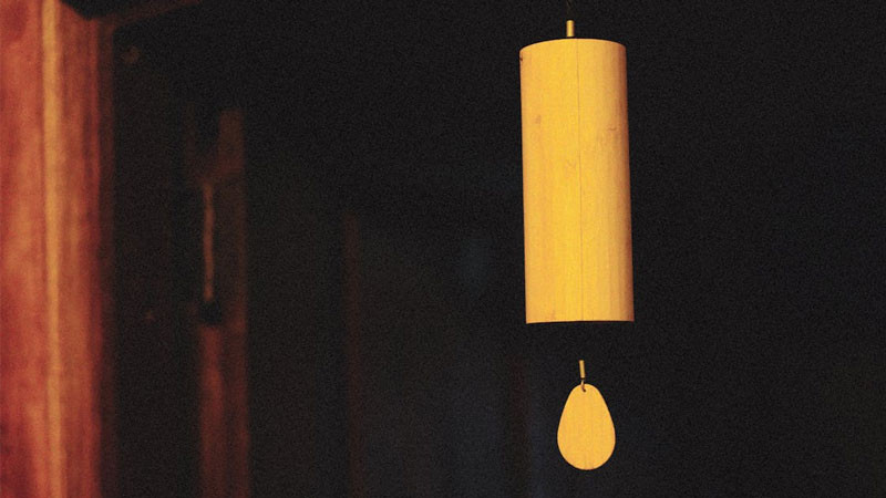 Hình ảnh chuông gió treo trên cành cây, rung động nhẹ nhàng trong gió