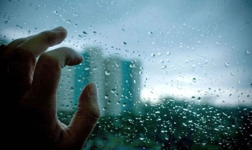 Hình ảnh một người che ô đi dưới trời mưa nặng hạt, thể hiện tâm trạng buồn và nặng lòng