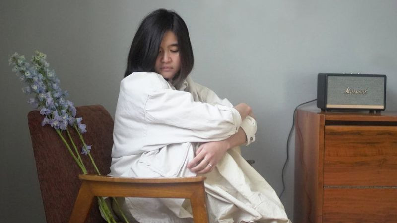 Hình ảnh một người ngồi cô đơn nhìn ra ngoài cửa sổ, thể hiện sự cách biệt và buồn bã