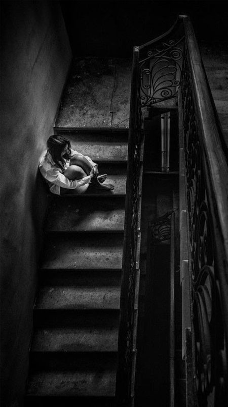 Hình ảnh một người phụ nữ ngồi một mình trong phòng trống, thể hiện sự cô đơn sâu sắc