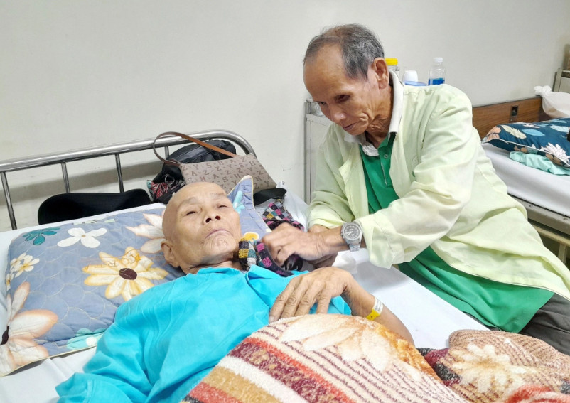 Hình ảnh người chồng ngồi cạnh giường bệnh chăm sóc vợ