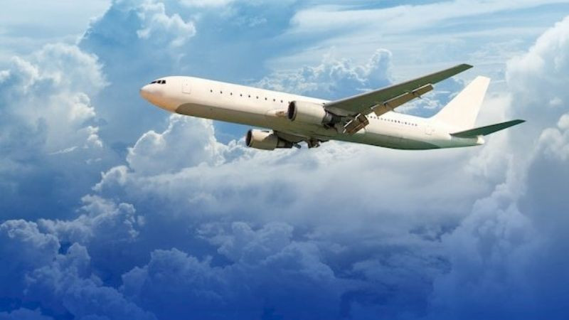 Máy bay đang bay ngang tầng mây, một phần thân máy bay bị mây che khuất, bầu trời phía trên đã trong xanh