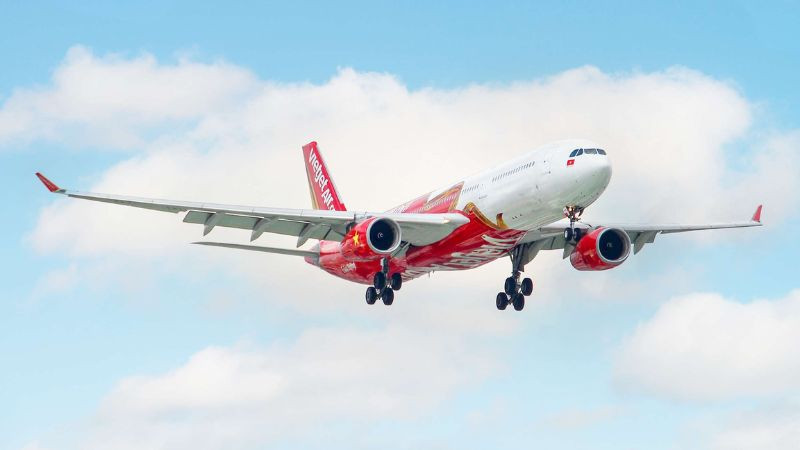 Máy bay màu đỏ trắng của hãng Vietjet Air đang vút lên, nhìn từ dưới lên với bầu trời xanh