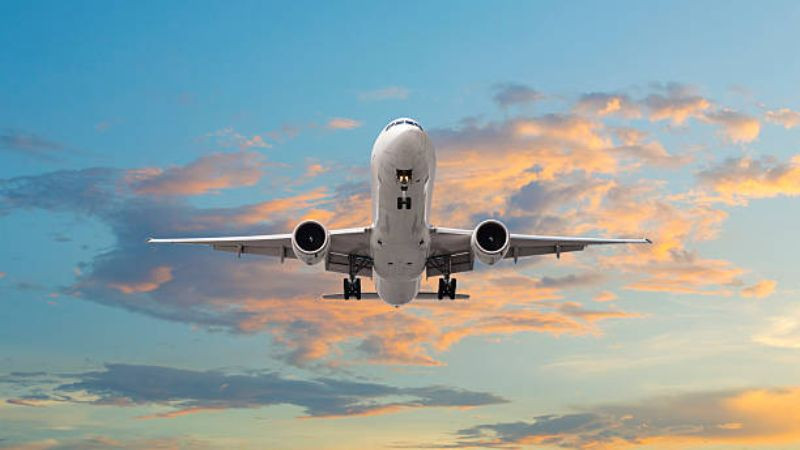 Máy bay phản lực đang cất cánh dưới ánh bình minh vàng cam, phía sau là dãy đèn đường băng