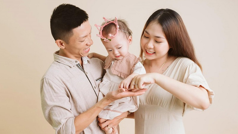 Mẹ và con gái nhìn nhau trìu mến, bố đứng sau ôm nhẹ