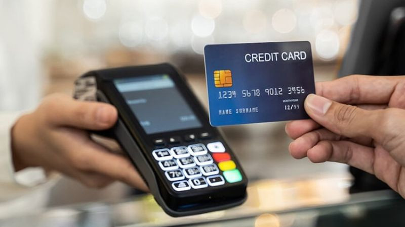 Một bàn tay đang đưa thẻ tín dụng vào máy POS để thực hiện thanh toán trực tiếp tại cửa hàng, minh họa cách sử dụng mã CVV/CVC trong giao dịch POS.