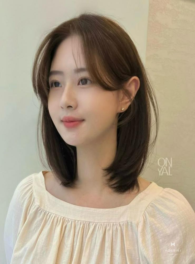 Một cô gái với mái tóc layer ngang vai đen thẳng tự nhiên và mái thưa, trông rất trẻ trung và tươi tắn.