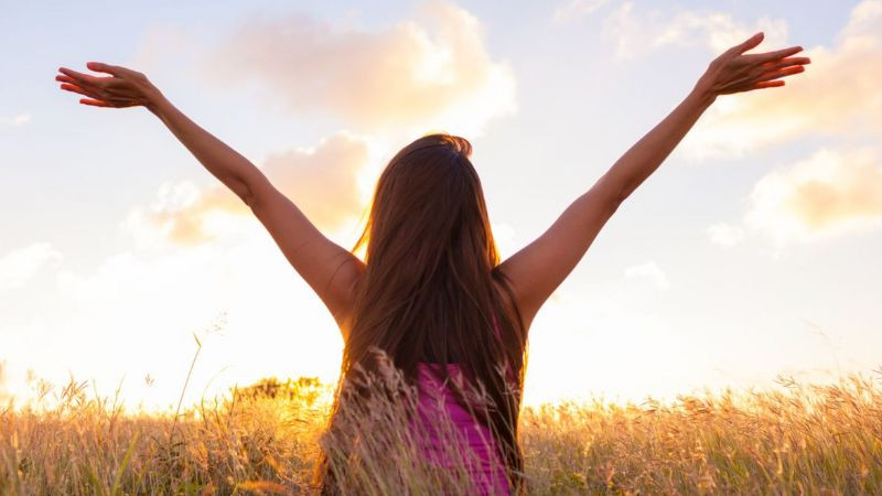 Một người dang rộng vòng tay bước đi trong công viên, thể hiện sự tự do, hạnh phúc và tác động tích cực của healing.