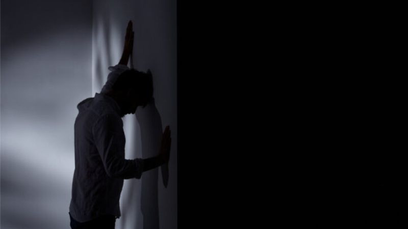 Một người ngồi dựa vào tường, đầu gục xuống, thể hiện sự đau khổ và bất lực