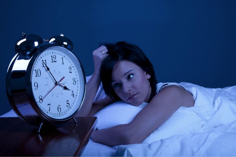 Người đang dùng điện thoại trên giường vào buổi tối, không ngủ được