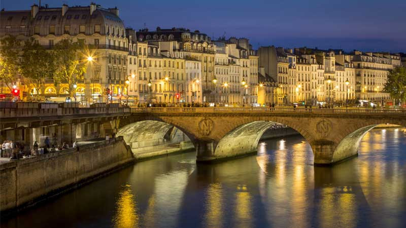 Tàu thuyền trên sông Seine lấp lánh ánh đèn khi đi qua Tháp Eiffel vào ban đêm