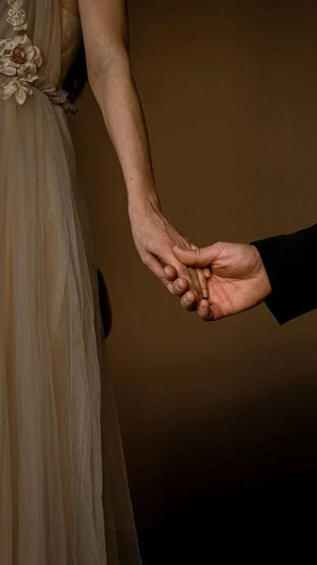 Tay nam và nữ nắm lấy nhau, cả hai đều đeo nhẫn cưới vàng