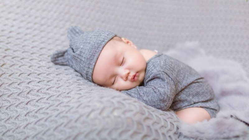 Trẻ nhỏ ngủ say trên ghế sofa, tay còn cầm đồ chơi