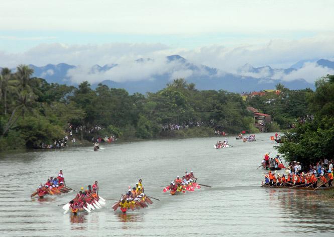 Bức tranh màu nước sống động về lễ hội đua thuyền trên sông với nhiều đội thuyền đang tranh tài quyết liệt