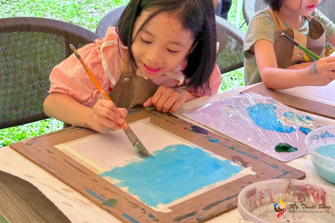 Bé gái đang chăm chú vẽ tranh với màu acrylic ngoài trời