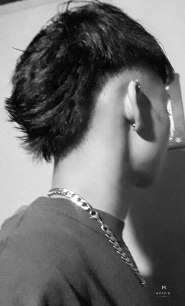 Giải Mã Sức Hút Của Kiểu Tóc Mohican Chéo Hiện Đại Chàng trai trẻ với tóc Mohican chéo màu nâu sáng đứng trước cửa sổ