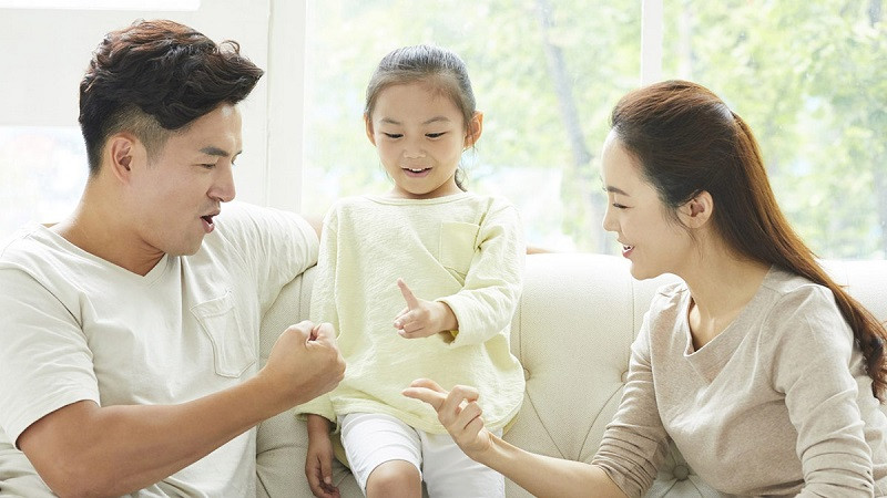 Gia đình 3 người mặc đồ trắng ngồi vui vẻ bên nhau